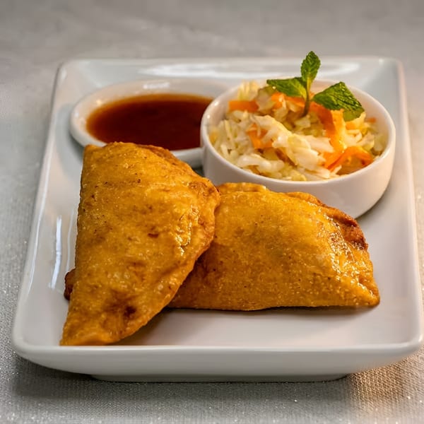 Two golden empanadas with coleslaw and dipping sauce on a white rectangular plate.