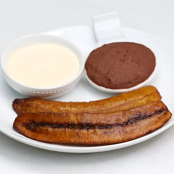 Two golden fried plantains served with bowls of light cream and dark chocolate sauce on a white plate.