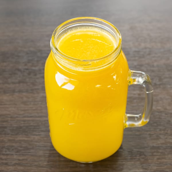 A mason jar mug filled with bright yellow juice sits on a dark wooden table.