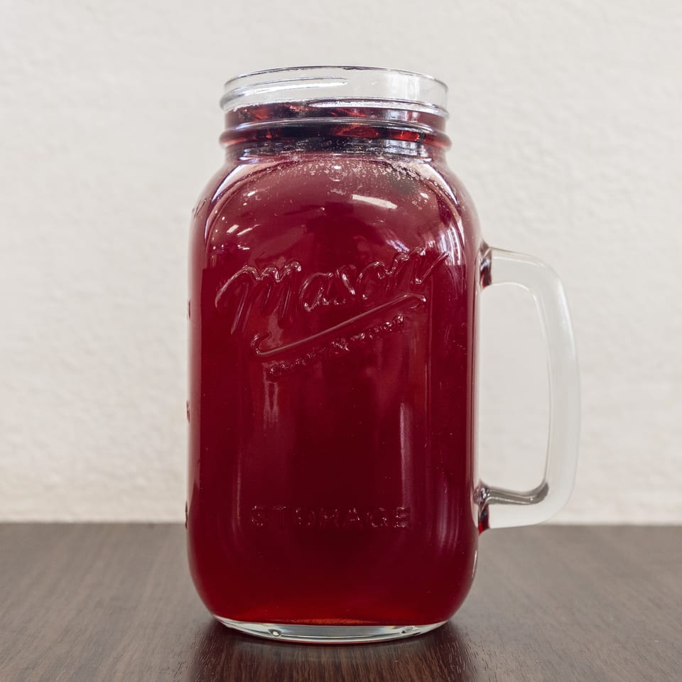 A Mason jar mug filled with a dark red beverage sits on a dark wooden surface.