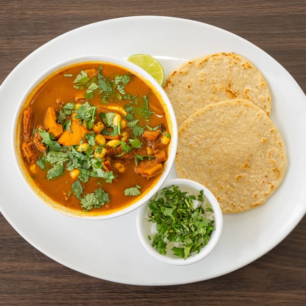 Hearty stew with sweet potatoes, corn, and cilantro, served with tortillas and lime.