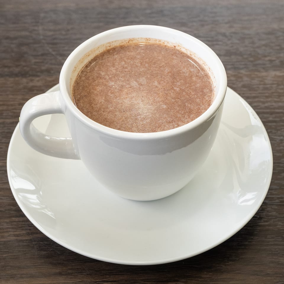 A white mug filled with hot chocolate, resting on a white saucer on a dark wooden table.