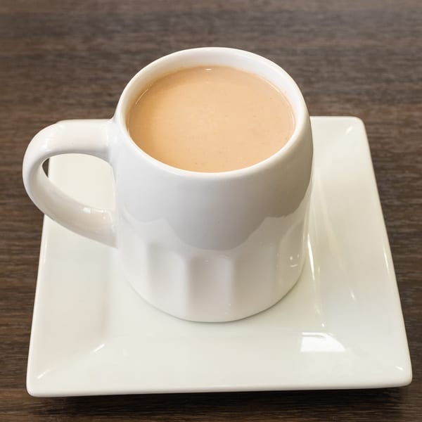 A white mug filled with light brown chai tea, resting on a white square saucer.