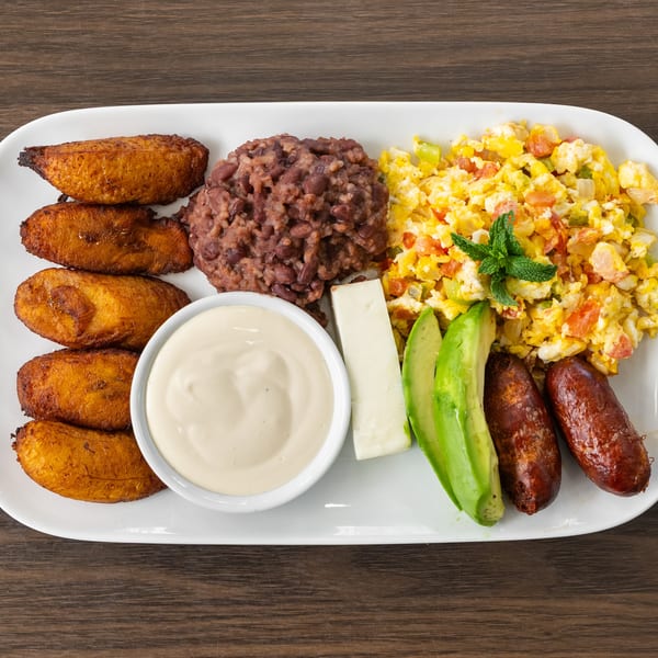 A white rectangular plate with fried plantains, rice and beans, scrambled eggs, avocado, cheese, and sausages.