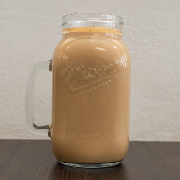 A glass mason jar mug filled with a light brown beverage, possibly iced coffee or tea.