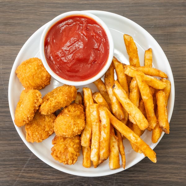 Crispy chicken nuggets, golden french fries, and a bowl of ketchup on a white plate.