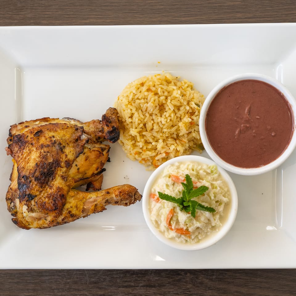Grilled chicken with rice, refried beans, and coleslaw with mint on a white rectangular plate.